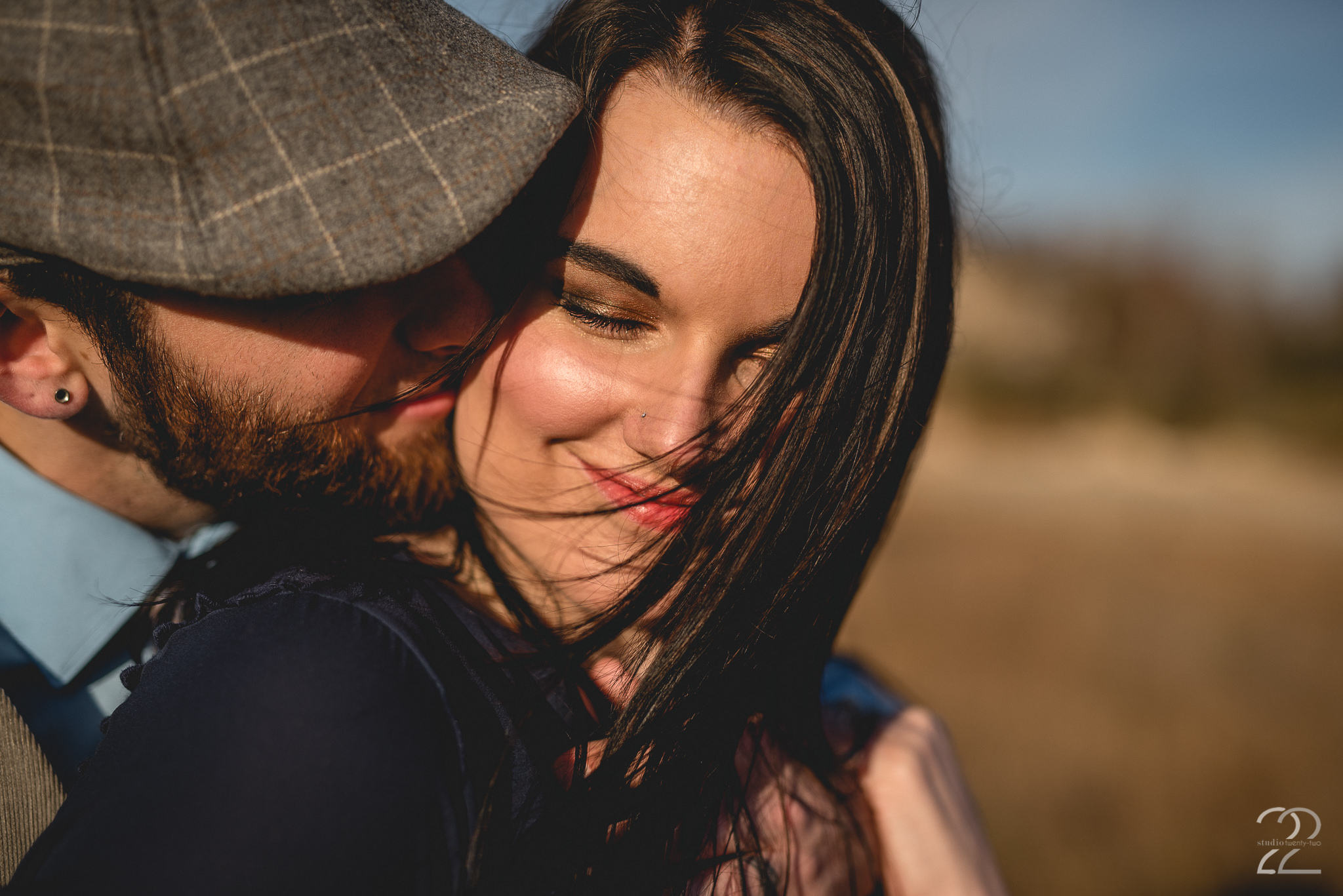 Up close photo of a man kissing a woman on the cheek as the wind blows the woman's hair across her face, smiling, at Oakes Quarry Park by Dayton Wedding Photographer Studio 22 Photography